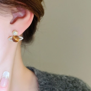Macro shot of gold planet stud earring with tiger eye stone and crystals on ear