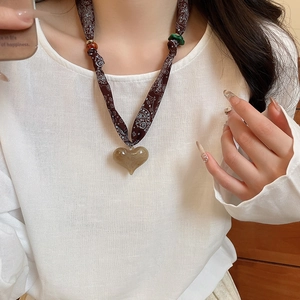 Detail of brown paisley fabric cord necklace featuring a beige resin heart-shaped pendant