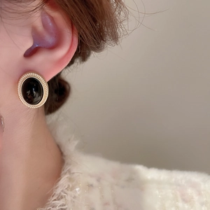 Close-up of a vintage gold-twisted oval earring with a black stone on a model