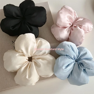 Detailed view of four colorful 3D floral silk satin scrunchies in black, pink, and blue