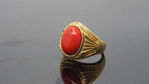 Close-up of golden titanium ring with oval red gemstone and textured band details