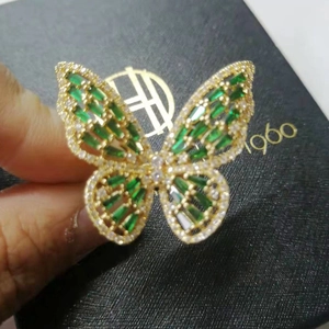 Macro detail of a golden butterfly ring featuring green emerald-cut stones and tiny diamonds