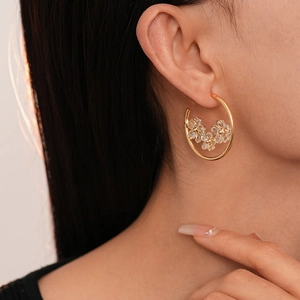 Gros plan de boucles d'oreilles créoles dorées en C ornées de trois fleurs en cristal