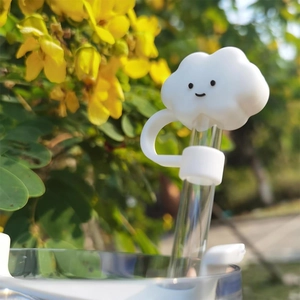 Close-up of white smiling cloud silicone straw cover on a glass straw in outdoor garden