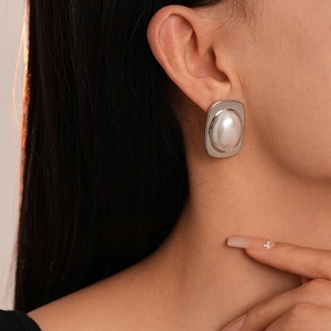 Close-up of a silver rectangular stud earring with a large pearl inlay on a female model