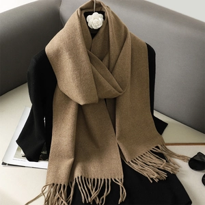 Detail of camel cashmere scarf with soft fringes styled over a black sweater