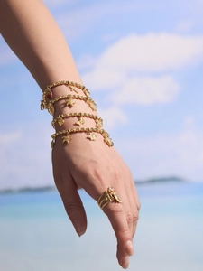Detail eines vergoldeten Armbands mit Seestern und Schmetterling am Strandhintergrund