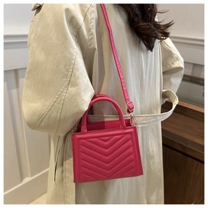 Magenta V-quilted lady bag with top handle worn over a beige trench coat for casual style