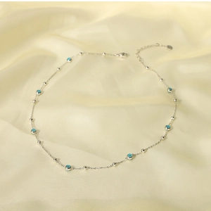 Detail view of silver necklace with blue evil eye beads and small silver beads on silk