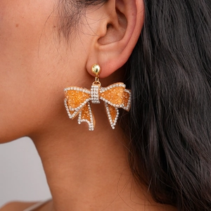 Macro view of orange resin bow earring with sparkling sugar texture and rhinestones