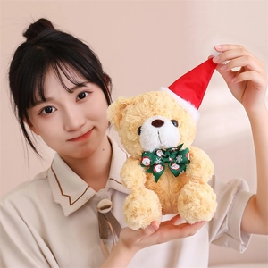 Detail of a plush teddy bear with a red Santa hat and green bow held by a person