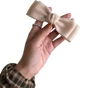 Elegant beige satin bow hair clip held by hand, minimalist spring fastener accessory