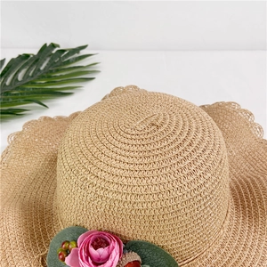 Détail d'un chapeau de paille beige avec bord ondulé et fleurs roses décoratives