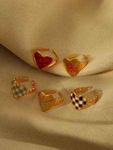 Set of five gold adjustable rings with colorful heart-shaped enamel designs on beige cloth
