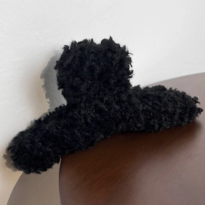 Close-up of black plush teddy fur hair claw clip with soft texture detail on wood table