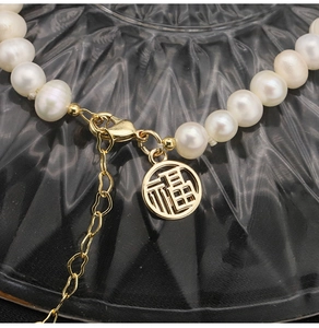 Macro shot of freshwater pearl necklace with gold Fu pendant and lobster clasp detail