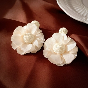 Détail de boucles d'oreilles fleurs en raphia blanc sur un fond de soie marron luxueux