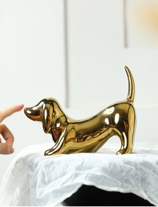 Polished gold ceramic dachshund statue detail on textured white fabric background