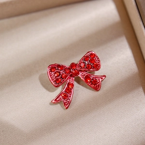 Detailed close-up of a red crystal bow brooch pinned on a beige fabric background