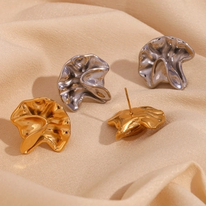 Irregular hammered gold and silver earrings with fold texture on beige fabric