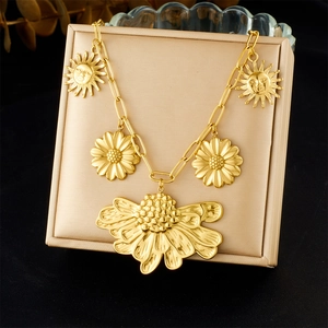 Close-up of gold stainless steel necklace featuring large flower and sun face pendants