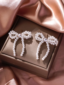Macro shot of elegant bow-shaped pearl tassel earrings on a champagne satin background