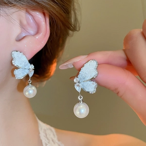Macro view of butterfly earrings with pearlescent wings and hanging pearl charm
