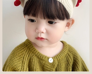 Close-up of baby girl wearing a cream knit hat with red pom-poms and green cardigan