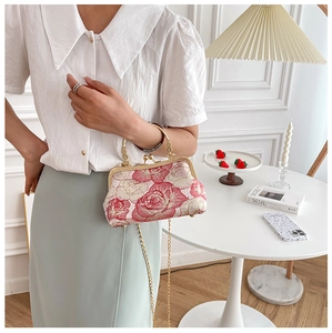 Detail of pink floral fabric handbag with gold chain strap held by a model