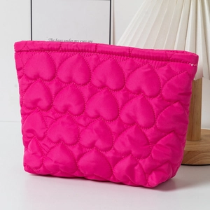 Pink heart quilted cosmetic bag with soft fabric texture shown on a minimal countertop