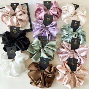 Flat lay of 11 oversized 18cm satin scrunchies in various vintage colors with handmade tags