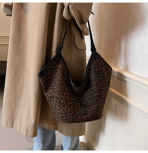 Detail of a large leopard print tote bag with black leather straps on a beige trench coat