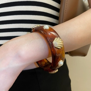 Dettaglio del bracciale in resina ambrata con conchiglia dorata e perle su braccio