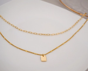 Detail of layered gold titanium necklace featuring a Good Luck engraved pendant