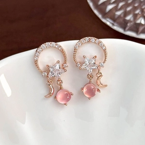 Macro view of rose gold moon and star drop earrings with a soft pink cat-eye bead