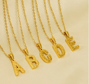 Detail view of 18K gold plated stainless steel letter necklaces A to E on fabric