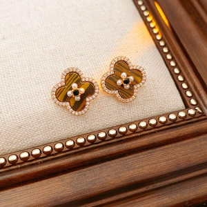 Macro detail of clover earrings with brown gemstone, pearls, and gold finish