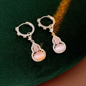 Macro shot of silver earrings with pink cat-eye stone gourd pendant on green velvet