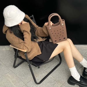Brown EVA tote bag with perforated hole design held by model in casual resort setting