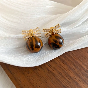 Detail of leopard print ball earrings with golden rhinestone bow on silk fabric