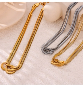 Detail of gold and silver double-layer snake chains with punk knot design on textured surface