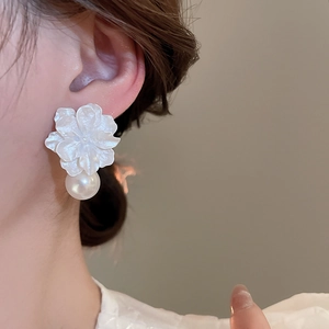 Close-up of white resin flower and pearl earrings worn by a model in soft lighting