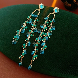 Detail of gold floral earrings with blue crystals and long turquoise beaded tassels