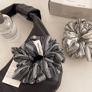 Close-up of a striped fabric scrunchie with handmade label on a leather bag