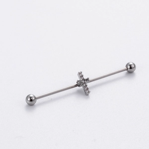 Macro detail of silver industrial barbell earring with a sparkling rhinestone cross charm