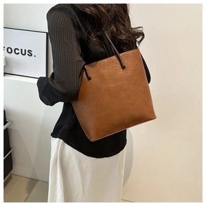 Brown vintage leather tote bag shown on a model's shoulder in a minimalist indoor setting