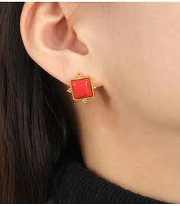 Macro detail of red natural stone square stud earring with gold beaded edge on model