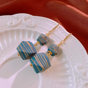 Close-up of vintage geometric blue-green striped beads and golden hooks on ceramic tray