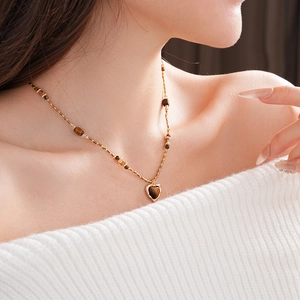 Gros plan d'un pendentif cœur en œil de tigre sur un collier de perles dorées pour femme
