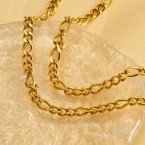 Polished gold stainless steel Figaro chain necklace displayed on a textured glass surface